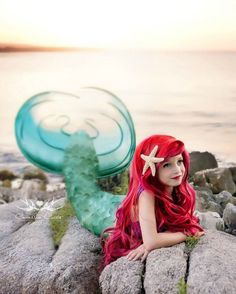 a woman with red hair sitting on rocks next to the ocean