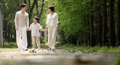 two adults and a child walking down a path in the woods with trees behind them