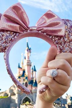 a person is holding up a minnie mouse ears headband in front of a castle