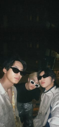 three young men wearing sunglasses are posing for the camera in front of a building at night