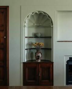 a vase with flowers sitting on top of a wooden cabinet next to a fire place