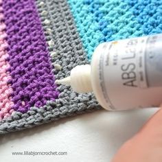 someone is crocheting on the side of a blanket with a bottle of glue