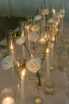 a table topped with lots of vases filled with white flowers and candles next to each other