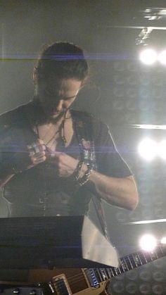 a man standing next to a guitar in front of a stage with lights on it