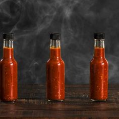 three bottles filled with hot sauce sitting on top of a wooden table