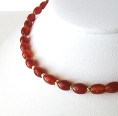 The Carnelian necklace features natural red orange oval barrel beads of carnelian gemstone accented with gold spacers and is one of a kind. It is finished with a goldfilled hook clasp and findings. The necklace can be fastened at collar (choker) length 16 inches and is adjustable to 18 inches with the extension chain. The Carnelian beads are translucent and a warm, deep red with colors of russet and orange. The color will appear darker when the necklace is against a surface or in low light; and Luxury Carnelian Faceted Beads Necklace, Red Carnelian Oval Pendant Necklaces, Red Carnelian Oval Pendant Necklace, Red Gemstone Necklace With Oval Beads, Orange Oval Carnelian Necklaces, Red Carnelian Oval Necklace, Oval Carnelian Necklace With Natural Stones, Red Oval Carnelian Necklace, Red Orange Color