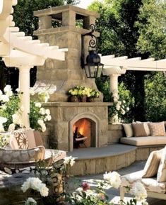 an outdoor fireplace with lots of seating around it and flowers on the table next to it