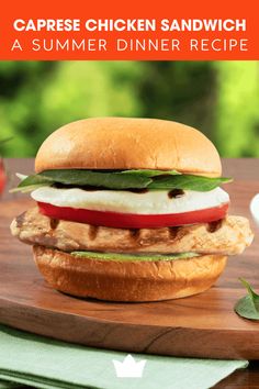 a chicken sandwich with lettuce and tomato on a cutting board next to an apple