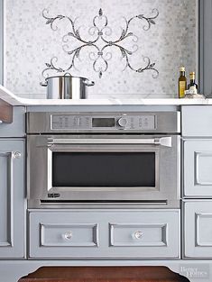 a kitchen with gray cabinets and white countertops has an oven built into the wall