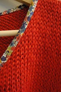 a red knitted fabric with flowers on it and a knitting needle in the middle