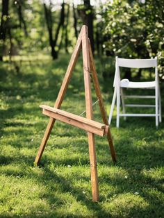 a wooden easel sitting in the grass next to a white chair