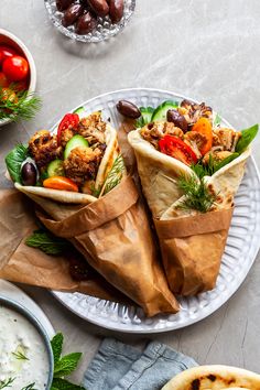 two wraps filled with meat, vegetables and sauces on a plate next to pita bread