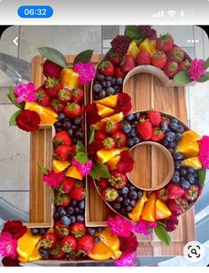 the number six made out of fruit is displayed on a wooden tray with flowers and berries