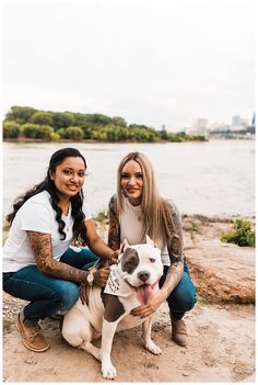 two women sitting next to each other with a dog in front of them on the beach