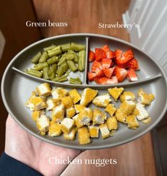 a person holding a plate with different types of food on it that includes green beans, strawberries and chicken nuggets