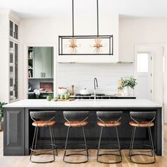 three bar stools sit in front of an island with four lights hanging over it