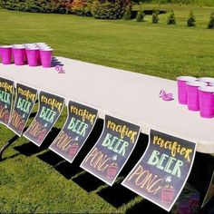 a long table with purple cups on it in the middle of a grassy field next to trees