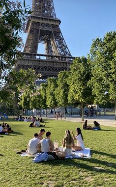 people sitting on the grass in front of the eiffel tower