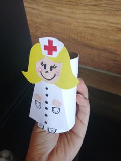 a paper doll with a red cross on it's head is held in front of a wooden table