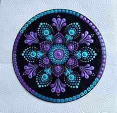 a black and purple circular design painted on a white surface with blue dots in the center