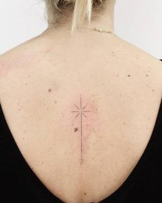 the back of a woman's neck with a small cross tattoo on her left shoulder