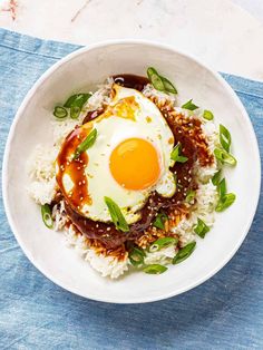 an egg on top of rice in a bowl with sauce and green garnish