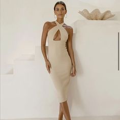 a woman standing in front of a white wall wearing a tan dress with cutouts