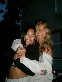 two beautiful young women hugging each other in front of a house at night with the lights on