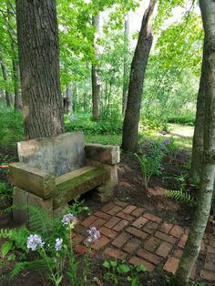 a stone bench sitting in the middle of a forest next to a brick walkway and trees