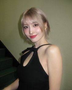 a woman in a black dress standing next to some stairs and looking at the camera