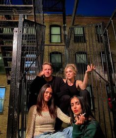 four people sitting on the steps of an apartment building at night, posing for a photo