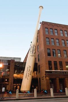 a large baseball bat is in front of a tall brick building with windows and lights