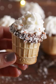 a hand holding an ice cream cone with chocolate sprinkles and white frosting