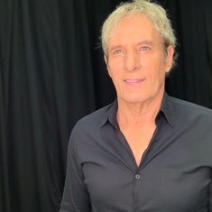 a man with blonde hair and blue eyes posing for a photo in front of black backdrop