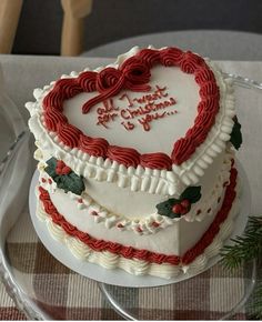 a heart - shaped cake on a glass platter is decorated with red and white icing