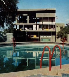 an empty swimming pool in front of a large apartment building with red railings on each side