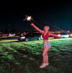 a woman holding a sparkler in her hand while standing on top of a grass covered field