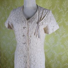 Ivory Lace lined in a soft cotton. This lovely vintage dress has short sleeves, buttons up the front with a snap at the waist and the top. The shoulder detail adds a quirky, unusual element and the same fabric is used to cover the buttons and for the piping at the neckline and front. The dress has a fitted bodice and features a slightly flared skirt hitting a below the knee. I picture this dress paired with gloves and a veiled fascinator.The label says Mann Mate Orginal.The lace is in great shap Retro Vintage Dress With Short Sleeves For Formal Occasions, Summer Short Sleeve Dresses For Vintage Events, Vintage Summer Dresses With Covered Buttons, Cream Short Sleeve Dress With Button Closure, Formal Short Sleeve Vintage Dress, Formal Vintage Short Sleeve Dress, Vintage Short Sleeve Dress With Covered Buttons, Vintage Dress With Covered Buttons And Short Sleeves, Cream Retro Vintage Dress With Short Sleeves