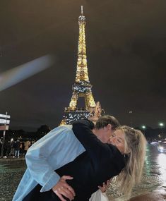 a man and woman are kissing in front of the eiffel tower at night