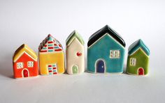 small ceramic houses are lined up on a white surface, one is painted multicolored