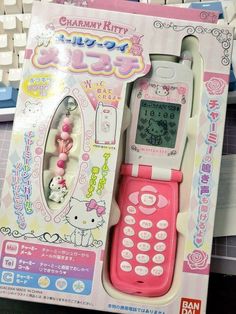 a pink and white cell phone with hello kitty on it's display stand in front of a keyboard