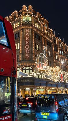 a red double decker bus driving past a tall building with christmas lights on it's side