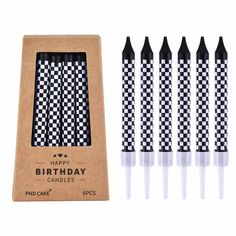 four black and white checkered candles in a cardboard box with the packaging next to it