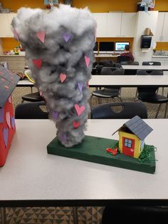 a house made out of clouds on top of a table in a room filled with desks