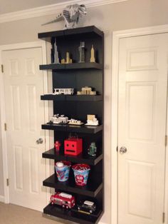 a black shelf in the corner of a room filled with toys and other items on top of it