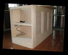 an unfinished kitchen cabinet with wires running through the bottom and below it, on a hard wood floor