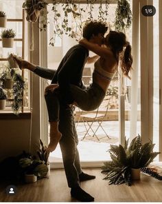 a man and woman dancing in front of a window with potted plants on the windowsill