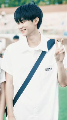 a young man with black hair wearing a white shirt and blue suspenders giving the peace sign