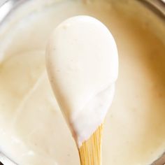 a wooden stick sticking out of a white sauce in a silver pot with some liquid