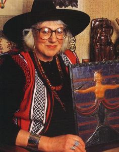 an older woman in a black hat holding a painting